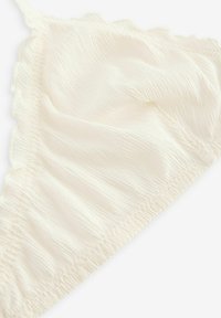 Krém színű bralette, texturált anyagból készült, fodros szélekkel és redőzött részletekkel az alsó szegélynél, amelyek további dimenziót adnak.