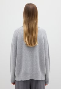 Hellgrauer, übergroßer Pullover aus weichem, strukturiertem Material mit gerippten Säumen und lockerem Schnitt. Kombiniert mit grauer Hose.