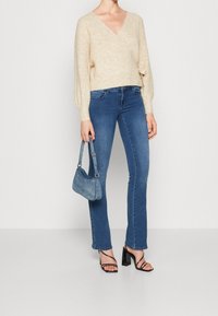 Beżowy, dziany sweter narzutowy; rozszerzane niebieskie dżinsy; czarne sandały na wysokim obcasie; niebieska torebka na ramię. Prosty design z miękkimi fakturami.