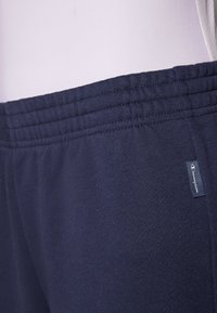 Tumši zili sporta bikses ar elastīgu jostu, maigu tekstūru un mazu logo uzlīmi sānos, ar vienkāršu un funkcionālu dizainu.