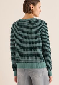 Grüner Strickpullover mit strukturiertem Muster, einschließlich eines gerippten Halsausschnitts und Bündchen sowie einer taillierten Passform. Die Rückansicht zeigt ein nahtloses Design.