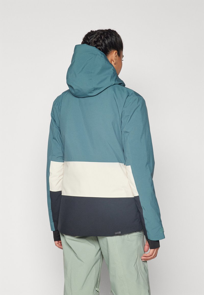 Teal wasserdichte Jacke mit Kapuze, die horizontale cremefarbene und marineblaue Farbkombinationen aufweist. Das Material hat eine glatte, matte Textur.