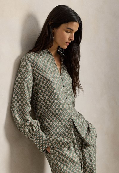 Πράσινη μπλούζα με σχέδια και γιακά, με μικρά λουλουδάτα μοτίβα. Μακριά μανίκια και κουμπιά μπροστά. Μαλακή, απαλή υφή υφάσματος.