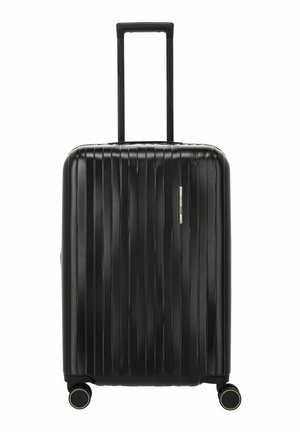 Maleta rígida negra con relieves verticales, asa telescópica extendida y cuatro ruedas dobles giratorias con detalles en dorado.