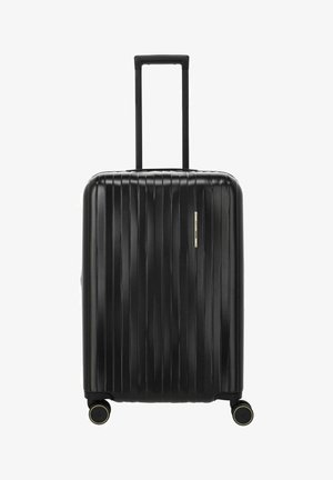 Valise rigide noire à rainures verticales, poignée télescopique déployée et quatre roues doubles pivotantes avec accents dorés.