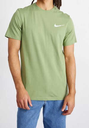 T-shirt in cotone verde con maniche corte e scollo rotondo. Presenta un logo Nike bianco sul lato sinistro del petto e una vestibilità comoda.