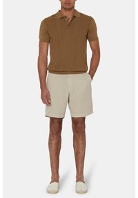 Polo shirt marrone lavorato a maglia con motivo a diamante, abbinato a pantaloni corti beige. Il modello indossa espadrillas chiare. Design semplice e su misura.