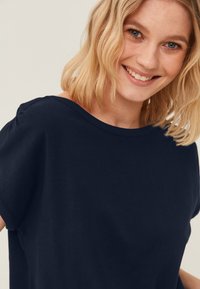 Mørkeblå kortærmet t-shirt lavet af blød bomuld. Har en afslappet pasform og bådhalsudskæring med diskret samling ved skuldersømmene.
