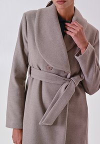 Cappotto avvolgente in misto lana beige con grande collare, maniche lunghe, cintura da annodare e chiusura con bottone davanti. Tessuto morbido.