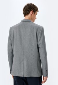 Graue Texturjacke mit taillierter Passform, einem Schlitz auf der Rückseite und knöpfbaren Manschetten. Glattes Material und elegantes Design.