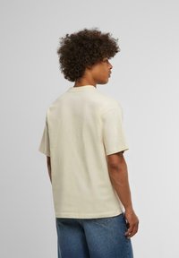 Kortærmet, lys beige t-shirt med en afslappet pasform, rund halsudskæring og glat tekstur. Minimalistisk design, ingen synlige mønstre eller accenter.