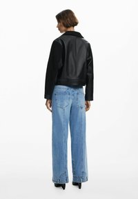 Zwart leren cropped jack met een matte afwerking, gecombineerd met lichtgewassen wijde jeans met grote achterzakken en stikseldetails.