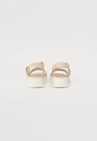 Sandales à plateforme beiges avec une tige en cuir lisse, des brides entrecroisées et une semelle blanche texturée. Vue de l'arrière.
