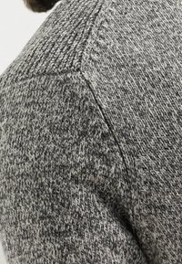 Grauer strukturierter Strickpullover mit einem dezenten Muster, ausgestattet mit einem Raglan-Ärmeldesign und weichem, kuscheligem Material.