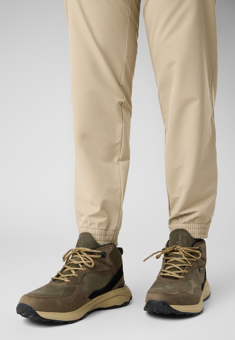 Bruine wandelschoenen van gestreept suede en mesh bovenkant, gecombineerd met beige, elastische onderbroek. Veters zijn lichtbruin en plat.