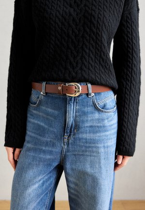 Brun læderbælte med en sølv oval spænde, båret over blå denimjeans og en struktureret sort striktrøje.