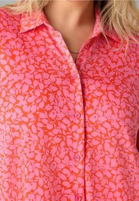 Košile s krátkým rukávem v zářivé korálové barvě s růžovým vzorem listů, s límečkem a zapínáním na knoflíky. Hladká textura látky.