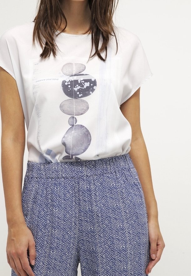 Top blanco con un estampado gráfico de piedras apiladas, combinado con pantalones holgados de color azul con un diseño de espiga.