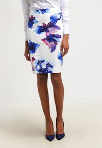 Floraler Bleistiftrock aus weißem Stoff mit Aquarellblumenmustern in Blau, Rosa und Lila; kombiniert mit marineblauen spitzen Schuhen.