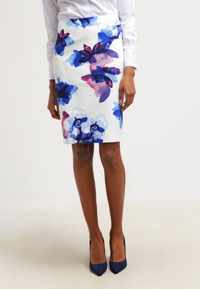 Floraler Bleistiftrock aus weißem Stoff mit Aquarellblumenmustern in Blau, Rosa und Lila; kombiniert mit marineblauen spitzen Schuhen.