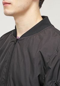 Black bomber jacket with a smooth, lightweight material. Features ribbed collar and zipper closure, showcasing a simple design.