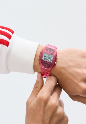 Persona che regola un orologio digitale rosa sul polso, indossando una manica bianca con strisce rosse. L'ora visualizzata è 17:09:36.