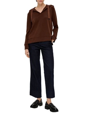Sweat-shirt à capuche brun avec un col en V, doté de cordons de serrage. Associé à un pantalon large en jean noir et des mocassins noirs.