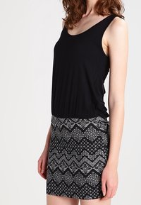 Débardeur noir à encolure dégagée associé à une jupe courte avec un motif géométrique noir et blanc. Tissu doux, design ajusté.