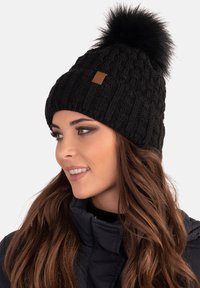 Berretto di maglia nero con texture a coste, dotato di un soffice pom-pom nero in cima e una piccola etichetta in pelle marrone sul lato.