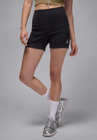 Svarta ribbade träningsshorts med hög midja och broderad vit logga på vänster ben. Bärs med vita strumpor och silverfärgade sneakers.