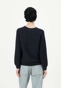 Ναυτικά μπλε πλεκτό πουλόβερ με μακριά μανίκια, ριγέ λαιμόκοψη και μανίκια, και άνετη εφαρμογή, συνδυασμένο με ανοιχτόχρωμα τζην παντελόνια.