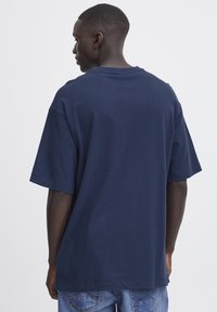 Tricou din bumbac de culoare bleumarin, supradimensionat, cu mâneci scurte, guler rotund și o textură netedă, văzut din spate.