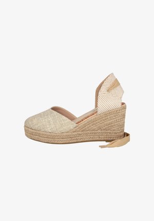 Alpargata cuña tejida beige con puntera cerrada, lazada en el tobillo y suela de plataforma con textura de cuerda, vista desde un lateral.