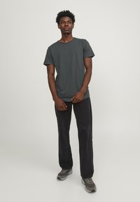 Camiseta de algodón gris oscuro con escote redondo, mangas cortas, combinada con pantalones de pierna ancha negros y zapatillas gris. Diseño simple y casual.