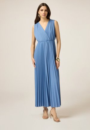 Langes, plissiertes Kleid aus leicht blauem Stoff mit V-Ausschnitt und ärmellosem Design, kombiniert mit beigen Riemchen-Highheels.