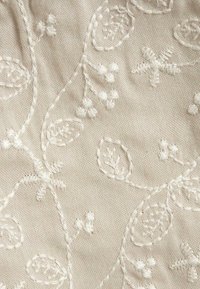 Un tissu crème présentant un riche broderie florale blanche avec des feuilles et des accents texturés. Texture douce et couture détaillée partout.
