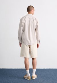 Light beige long-sleeve shirt with button cuffs, paired with cream-colored shorts. Worn with white socks and brown sneakers.