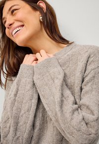 Beżowy sweter dzianinowy z fakturowanym wzorem, z prążkowanymi mankietami i okrągłym dekoltem. Miękki, przytulny materiał.