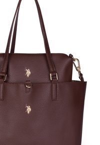 Borsa a spalla in pelle marrone con superficie ruvida, dotata di doppie maniglie, dettagli in metallo dorato e logo impresso. Presenta una forma strutturata e una finitura testurizzata.