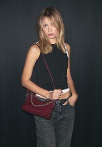 Borsa bordeaux con dettagli in catena, texture liscia e forma rettangolare. Il modello indossa una canotta nera e jeans a vita alta grigi.