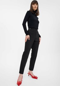 Crna dolga majica s dugim rukavima uparenjena s crnim hlačama visokog struka koje imaju bočne gumbe. Outfit dodatno ukrašavaju sjajne crvene sandale na petu s otvorenom petom.