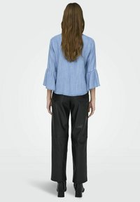 Haut en denim bleu clair avec des manches évasées, associé à un pantalon large en cuir synthétique noir et des bottines noires. Vue arrière de la tenue.