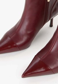 Stivaletti alla caviglia in pelle bordeaux con finitura lucida, punta affusolata e tacco stiletto sottile; dotati di una cerniera laterale per la chiusura.