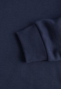 Tessuto della felpa blu navy con polsini a costine, caratterizzato da una texture liscia e un design senza cuciture. Il materiale sembra morbido e resistente.