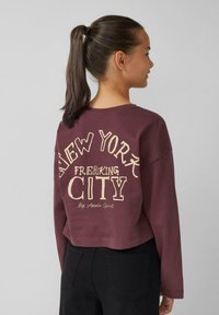 Bordeaux cropped sweatshirt met de tekst "NEW YORK FREAKING CITY" in crème. Lange mouwen, zachte textuur en een relaxte pasvorm.