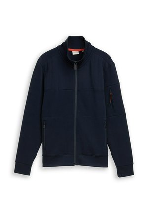 Giacca blu navy con zip e colletto alto, polsini a costine, tasche con zip frontali e sulle maniche, distesa su sfondo bianco.