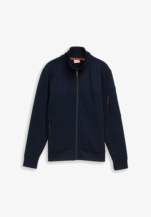 Giacca blu navy con zip e colletto alto, polsini a costine, tasche con zip frontali e sulle maniche, distesa su sfondo bianco.