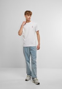 Vit bomull t-shirt med en liten rosa och blå grafik. Kombinerad med ljusblå jeans och metalliska sneakers. Enkel design och avslappnad passform.