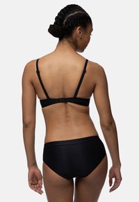 Melna bikini komplekts ar struktūrētu materiālu, regulējamām siksnām un slēgšanu aizmugurē topam, apvienots ar vidēji augstiem apakšējiem.