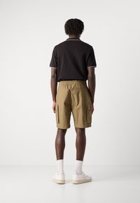 Polo nero con accenti bianchi, pantaloni cargo color khaki con due tasche laterali e sneakers bianche con logo. Modello visto da dietro.